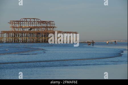 Les gens qui se promènent tôt le matin sur la plage à marée basse, avec les vestiges rouillés de West Pier, un quartier délabré de Brighton. Brighton & Hove, Sussex, Angleterre, Royaume-Uni Banque D'Images