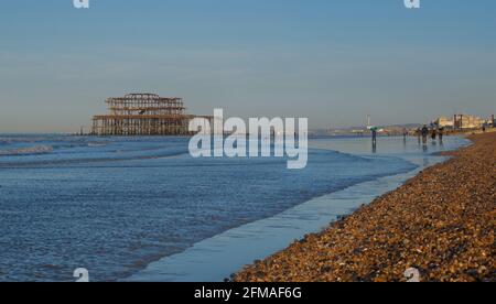 Les gens qui se promènent tôt le matin sur la plage à marée basse, avec les vestiges rouillés de West Pier, un quartier délabré de Brighton. Brighton & Hove, Sussex, Angleterre, Royaume-Uni Banque D'Images