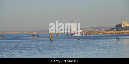 Les gens se promènent tôt le matin sur la plage à marée basse. Brighton & Hove, Sussex, Angleterre, Royaume-Uni. Vers l'ouest en direction de Shoreham, la centrale électrique au loin. Banque D'Images