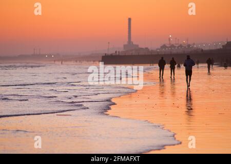 Brighton et la plage de Hove à marée basse, en direction de l'ouest vers la station électrique de Shoreham. Silhouettes de personnes marchant le long de la plage de sable au coucher du soleil. East Sussex, Angleterre Banque D'Images