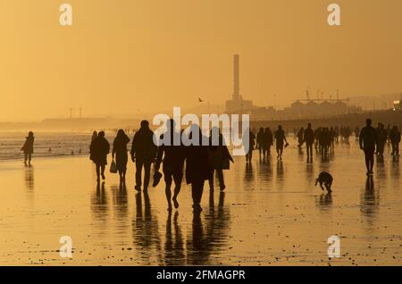 Brighton et la plage de Hove à marée basse, en direction de l'ouest vers Shoreham. Silhouettes de personnes marchant le long de la plage de sable au coucher du soleil. East Sussex, Angleterre Banque D'Images