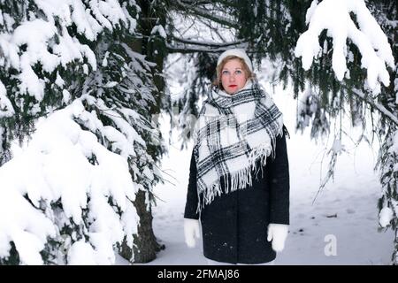 En hiver, une femme blonde se tient sous un sapin dans la neige. Banque D'Images