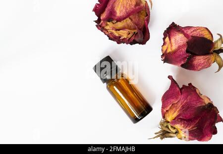 Bouteille avec huile de rose et roses séchées sur fond blanc Banque D'Images