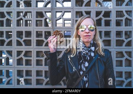 Jolie femme blonde aux cheveux tient une grande pomme de pin contre géométrique treillis Banque D'Images