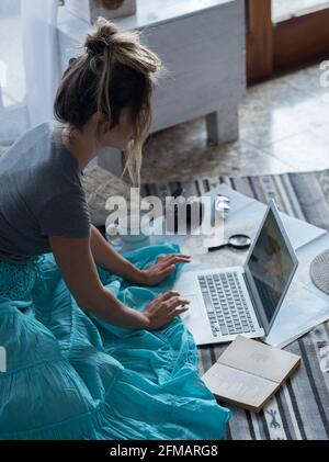 Femme caucasienne planifiant des voyages de vacances avec ordinateur portable et Internet à la maison, lisant le blog touristique en ligne dans Internet tout en se relaxant sur le sol Banque D'Images