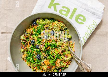 Un bol gris avec une salade de brocoli de couleur et une serviette de cuisine étiquetée 'kale' (chou). Banque D'Images