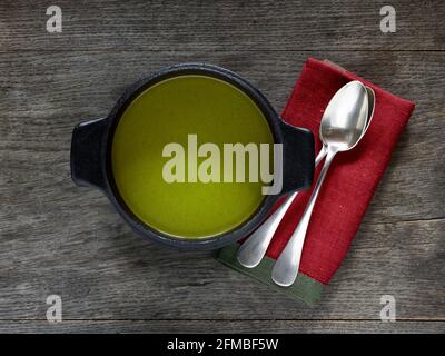 Cuisine ayurvédique - soupe de feuilles de chou-rave dans une casserole noire en fonte sur une table en bois, à côté d'une serviette rouge et de deux cuillères à soupe argentée Banque D'Images