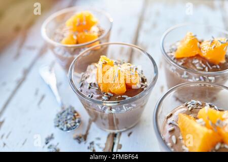 Cuisine ayurvédique - mousse au chocolat avec tofu silken, décorée de filets d'orange et de fleurs de lavande, de petits bols en verre remplis sont placés sur une table en bois blanc Banque D'Images