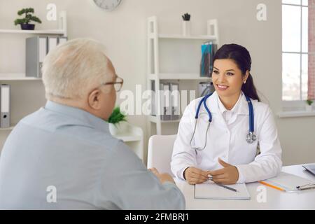 Femme souriante médecin à l'écoute d'un patient âgé pendant une entrevue médicale dans son bureau Banque D'Images