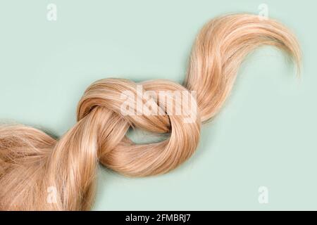 Boucle de cheveux blonds nouée. Brin de cheveux blond miel sur fond de menthe, vue du dessus. Service de coiffure, force des cheveux, coupe de cheveux, coiffure, mourir Banque D'Images