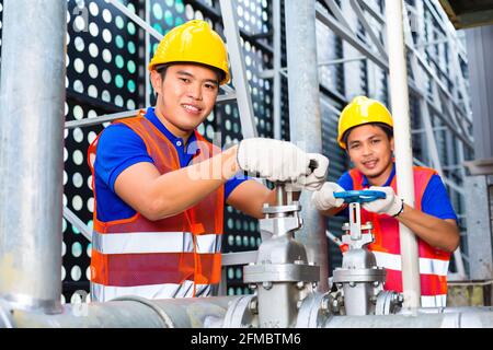 Deux techniciens ou ingénieurs travaillant sur une vanne sur la construction d'équipement technique ou site industriel Banque D'Images