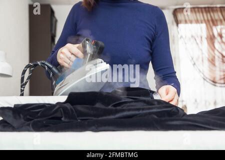 Couturière vole une veste de velours avec un fer dans son atelier. Style de vie authentique. Banque D'Images