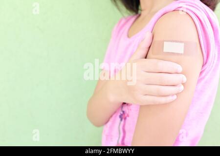 Gros plan de l'épaule d'une jeune fille asiatique vaccinée avec bandage adhésif dans le pouce vers le haut. Vaccination des jeunes enfants et des enfants contre le vaccin Covid-19. Banque D'Images