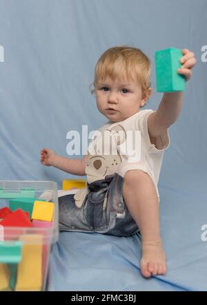 Une petite fille blonde dans une combinaison courte avec un répétition et lecture avec le constructeur de cubes colorés Banque D'Images