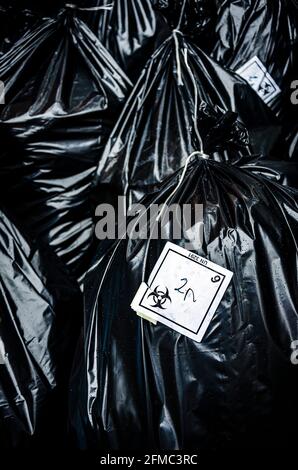 Sacs noirs jetables pour déchets biologiques dangereux avec logo sur les autocollants, déchets hospitaliers dans la rue par temps pluvieux Banque D'Images