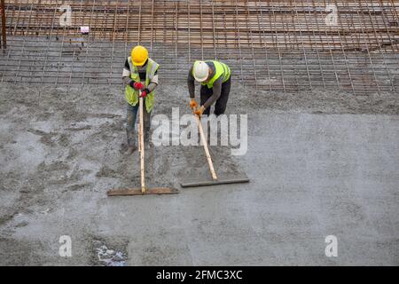 Les ouvriers des bottes en caoutchouc se trouvent dans le béton et dans le nivellement, en étalant les coulées. Banque D'Images