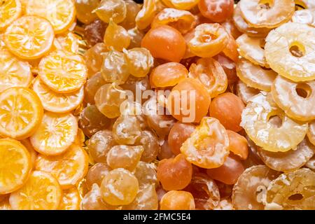 Tranches d'agrumes confites, fruits à noyau dorés et rondelles d'ananas disposées en rangées sur un marché de Barcelone, Espagne, avec un glaçage sucré brillant. Banque D'Images