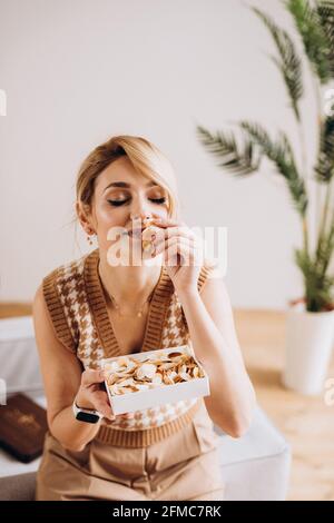 Belle femme blonde avec une boîte cadeau dans ses mains avec des confettis push-pop. Cadeau d'anniversaire, fête des femmes, fête des mères. Mise au point douce sélective, flou artistique, Banque D'Images