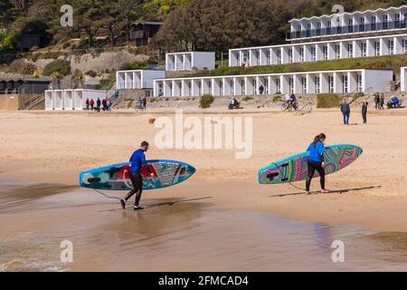 Surfeurs transportant des planches de surf planches de surf le long de la plage à Branksome Chine, Poole, Dorset Royaume-Uni en mai Banque D'Images