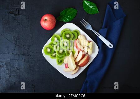 Dans une assiette sur une table en bois, mélanger des kiwis frais et des pommes avec des raisins. Banque D'Images