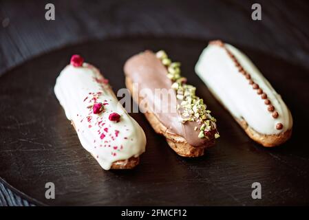 Dessert français eclairs ou profiteroles avec glaçage au chocolat et différentes garnitures sur une assiette en pierre noire. Pâtisseries crème anglaise et crème. Sélection logicielle Banque D'Images