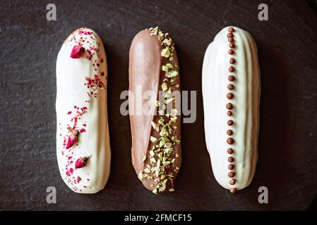 Dessert français eclairs ou profiteroles avec glaçage au chocolat et différentes garnitures sur une assiette en pierre noire. Pâtisseries crème anglaise et crème. Sélection logicielle Banque D'Images