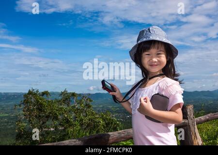 Bonne fille asiatique souriante au point de vue sur la montagne. Apprentissage des enfants prendre des photos paysage ciel bleu et fond de nature nuageux. Enfant relaxant ou Banque D'Images