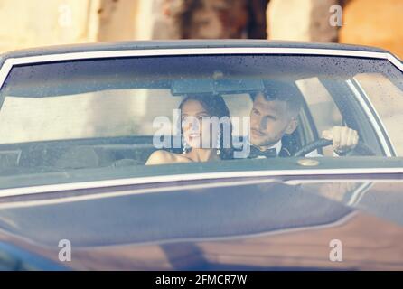 Elégante mariée et belle mariée embrassant dans une voiture élégante. Couple de mariage de luxe dans un style rétro. Banque D'Images