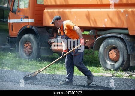 Mihaltsi, Bulgarie - Mai 7 2021: Un ouvrier nivelant l'asphalte avec un luth en bois Banque D'Images