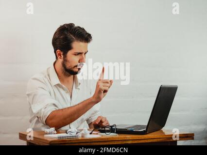 Jeune homme caucasien faisant le geste de déni tout en ayant une vidéo appel pendant le travail Banque D'Images