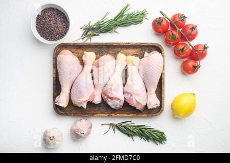 Pilons de poulet frais, jambes avec ingrédients pour la cuisson, avec romarin, épices et légumes, sur fond blanc, plan de dessus de lit plat Banque D'Images