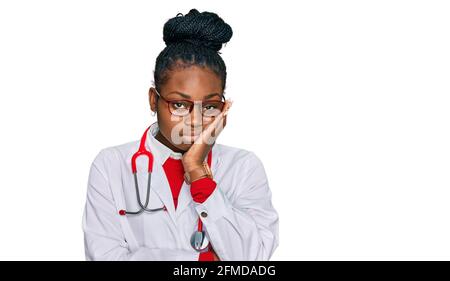 Jeune femme afro-américaine portant l'uniforme de médecin et le stéthoscope pensant fatigué et ennuyé avec des problèmes de dépression avec les bras croisés. Banque D'Images