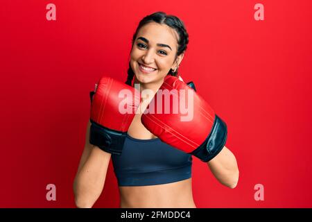 Jeune fille de brunette utilisant des gants de boxe souriant avec un sourire heureux et frais sur le visage. Montrant les dents. Banque D'Images