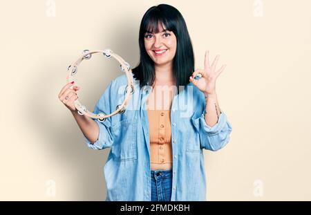 Jeune femme hispanique de taille plus jouant tambourine faisant signe ok avec les doigts, souriant sympathique gestante excellent symbole Banque D'Images