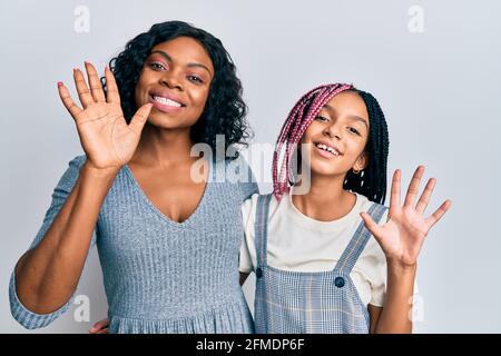 Belle mère et fille afro-américaine vêtue de vêtements décontractés et se moque de dire bonjour heureux et souriant, geste de bienvenue amical Banque D'Images