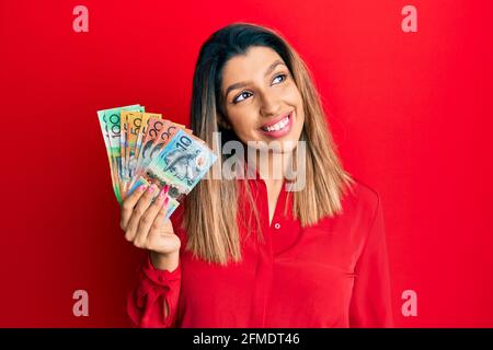 Belle femme brune tenant des dollars australiens souriant regardant à côté et regardant loin de penser. Banque D'Images