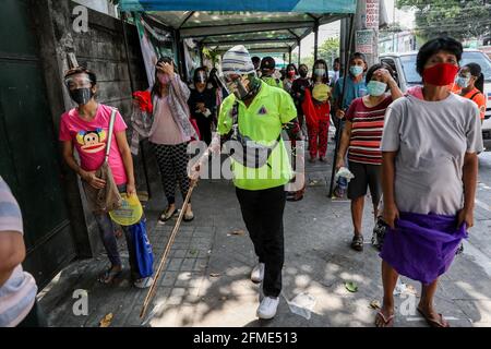 Un fonctionnaire du village suit une file d'attente de résidents qui attendent de recevoir gratuitement de la nourriture et d'autres produits dans un garde-manger de la communauté dans le quartier Maginhawa de Quezon City. Malgré les allégations des agents de la loi en tant qu'organisations communistes souterraines qui veulent saper le gouvernement, des pantares communautaires ont germé à travers le pays la semaine dernière pour aider les personnes touchées par des mesures strictes de quarantaine afin de freiner la propagation de la coronavirus. Metro Manille, Philippines. Banque D'Images