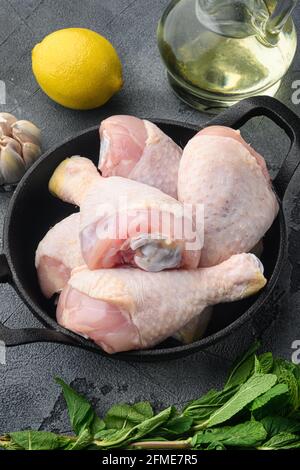 Pilons de poulet frais, jambes avec ingrédients pour la cuisson, sur poêle à frire en fonte, sur fond gris Banque D'Images