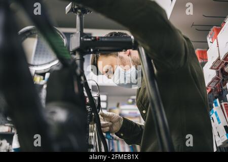 Atelier de vélo le réparateur travaille dans l'atelier d'entretien et de réparation de vélo pendant la quarantaine du coronavirus portant un écran facial et des gants, nouvelle norme. Mécanicien Banque D'Images