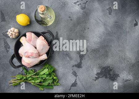 Des cuisses de poulet frais et des ingrédients de la marinade, sur une poêle à frire en fonte, sur fond gris, sur une surface plane avec vue de dessus, avec un espace pour le texte Banque D'Images