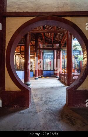 Fengdu, Chine - 8 mai 2010 : ville fantôme, sanctuaire historique. Porte circulaire ouvrant sur le sanctuaire bouddhiste avec des statues dorées derrière des fenêtres en verre. Banque D'Images