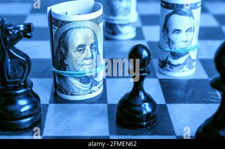 Billets et échecs en dollars, argent américain sur échiquier en lumière bleue. Les symboles et le jeu de la finance. Concept de la stratégie monétaire, de l'investissement, de la concurrence déloyale d'échecs Banque D'Images