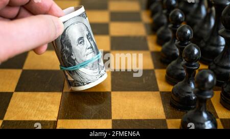 Jeu d'échecs et billets en dollars roulés comme mouvement blanc, argent américain sur l'échiquier. Billets américains et chiffres des échecs. Concept de stratégie d'entreprise, dollar l Banque D'Images