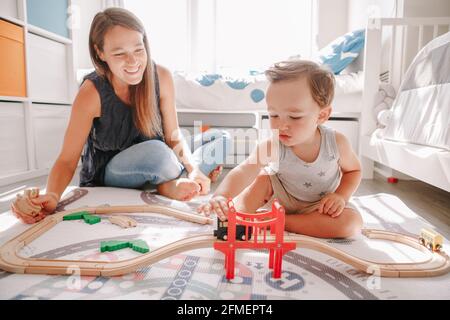 Mère et tout-petit garçon jouant avec une voiture de chemin de fer en bois sur le sol à la maison. Développement de l'éducation des jeunes enfants. Les enfants construisent la voie ferrée Banque D'Images