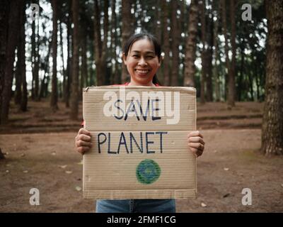 La jeune femme aux bannières protestant contre la pollution et le réchauffement climatique dans la forêt pour sauver la planète. Le concept de la Journée mondiale de l'environnement. Banque D'Images