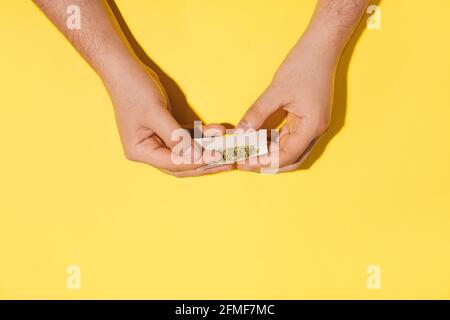 Les mains de l'homme roulent le cannabis sec ou des fumes à base de plantes sur fond jaune hipster. Pose à plat. Banque D'Images