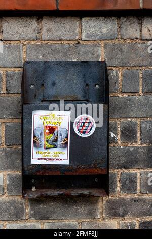 Deux autocollants sur un bac à déchets brisé et abandonné fixé à un mur de briques. Banque D'Images