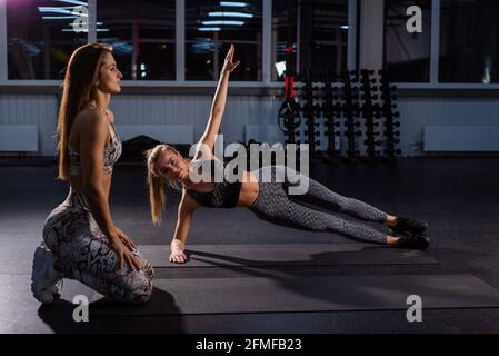 Une formatrice féminine apprend au service à exécuter correctement la barre latérale. Une entraîneuse féminine s'assure que son client, une jeune blonde, exécute le Banque D'Images