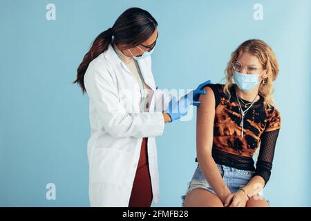 Femme médecin donnant le vaccin à la jeune femme. Un professionnel de la santé et un patient portant un masque facial pendant la vaccination. Vaccination pendant la pandémie de Covid-19 Banque D'Images