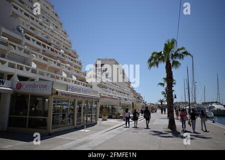 Touristes marchant sur un front de mer pavé à proximité de maisons blanches comme des vagues à la Grande Motte, près de Montpellier, Occitanie, sud de la France Banque D'Images